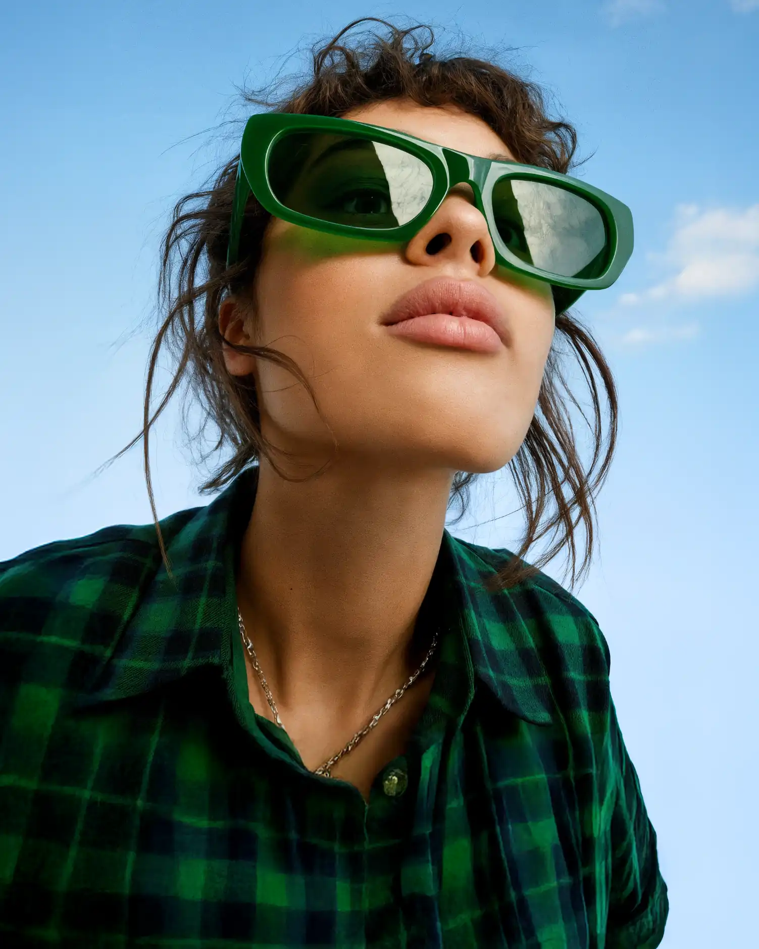 Une personne aux lunettes de soleil vertes lève les yeux vers un ciel bleu